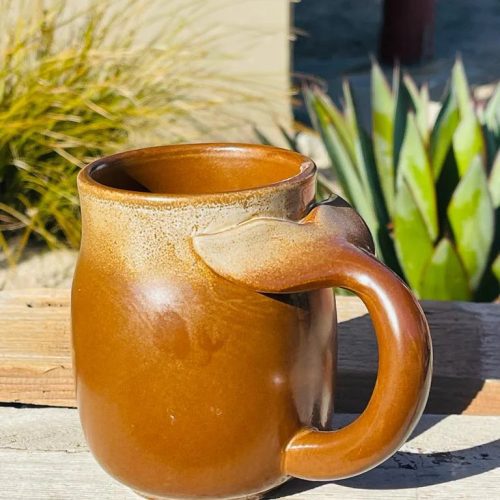 Brown stoneware mug with whale tail handle on a wooden table