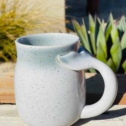 White stoneware mug with a whale tail handle placed on a wooden table