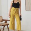 Woman showcasing BELTED ASYMMETRIC WAISTBAND SNAP BUTTON PANTS in empty room