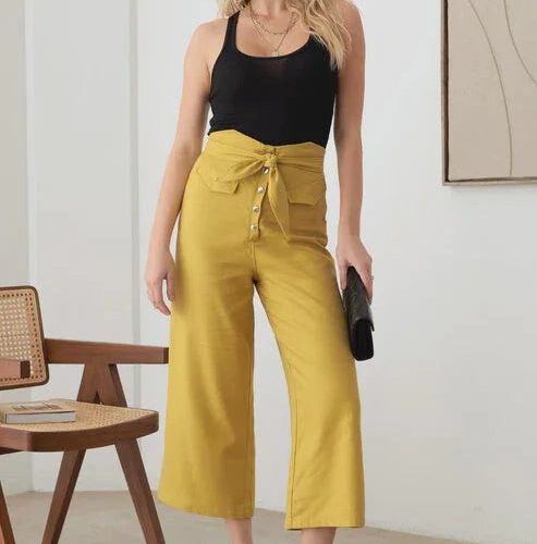 Woman showcasing BELTED ASYMMETRIC WAISTBAND SNAP BUTTON PANTS in empty room