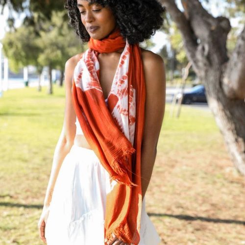 Woman in a white dress showcasing a tie dye lightweight scarf in vibrant orange